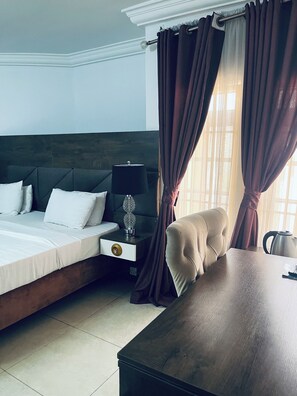 A hotel room with a bed, bedside table, lamp, and a view through curtains. - Top rank hotels galaxy wuse zone 4 (Abuja)