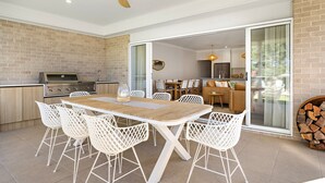 An outdoor dining area with a brick wall, a grill, and a sliding glass door leading to a living space. - Poppy's - Fire Pit - 4 Mins Walk to Beach (Callala Beach)
