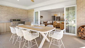 An outdoor dining area with a brick wall, a grill, and a sliding glass door leading to a living space. - Poppy's - Fire Pit - 4 Mins Walk to Beach (Callala Beach)