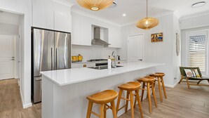 A modern kitchen with a large island, stainless steel appliances, wooden stools, and pendant lighting. - Poppy's - Fire Pit - 4 Mins Walk to Beach (Callala Beach)