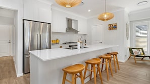 A modern kitchen with a large island, stainless steel appliances, wooden stools, and pendant lighting. - Poppy's - Fire Pit - 4 Mins Walk to Beach (Callala Beach)