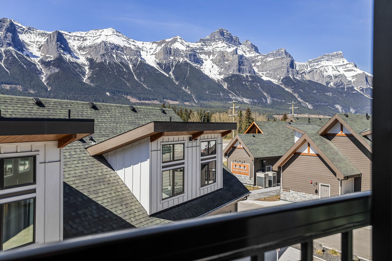 Un chalet de montagne composé de plusieurs bâtiments de style chalet, une enseigne indiquant « Sky Ridge », et des montagnes enneigées en arrière-plan.