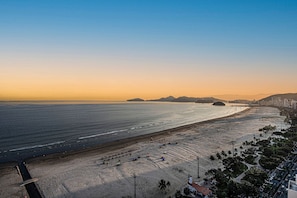 Un paisaje urbano costero con una playa extensa, cielo despejado y montañas lejanas.