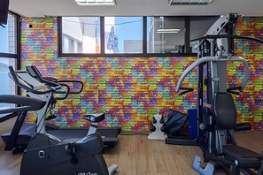 A gym with exercise equipment, a colorful brick-patterned wall, and a window with a view of buildings. - SHB -Santos Piscina Academia e Vista Mar (Santos)