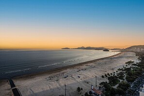 Un paisaje urbano costero con una playa extensa, cielo despejado y montañas lejanas.