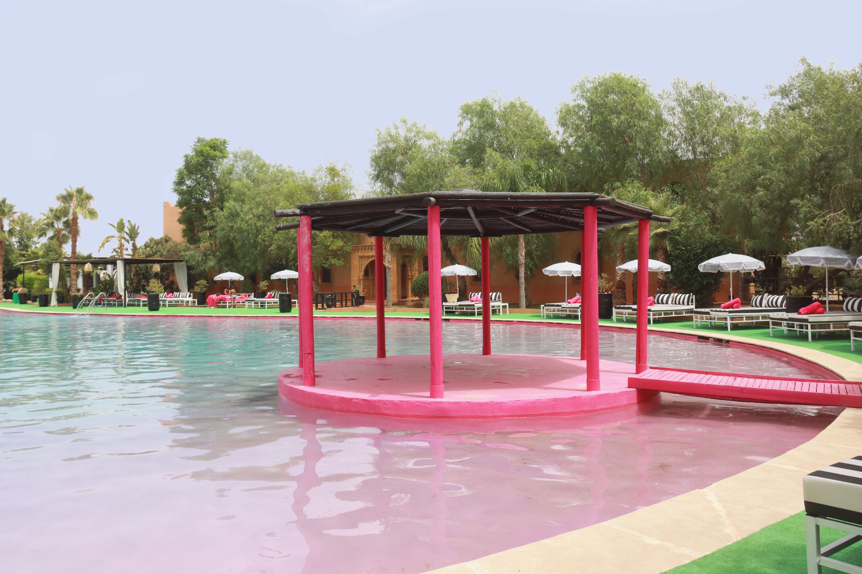 A pool area with a pink structure, lounge chairs, and umbrellas.