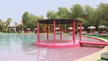 A pool area with a pink structure, lounge chairs, and umbrellas.