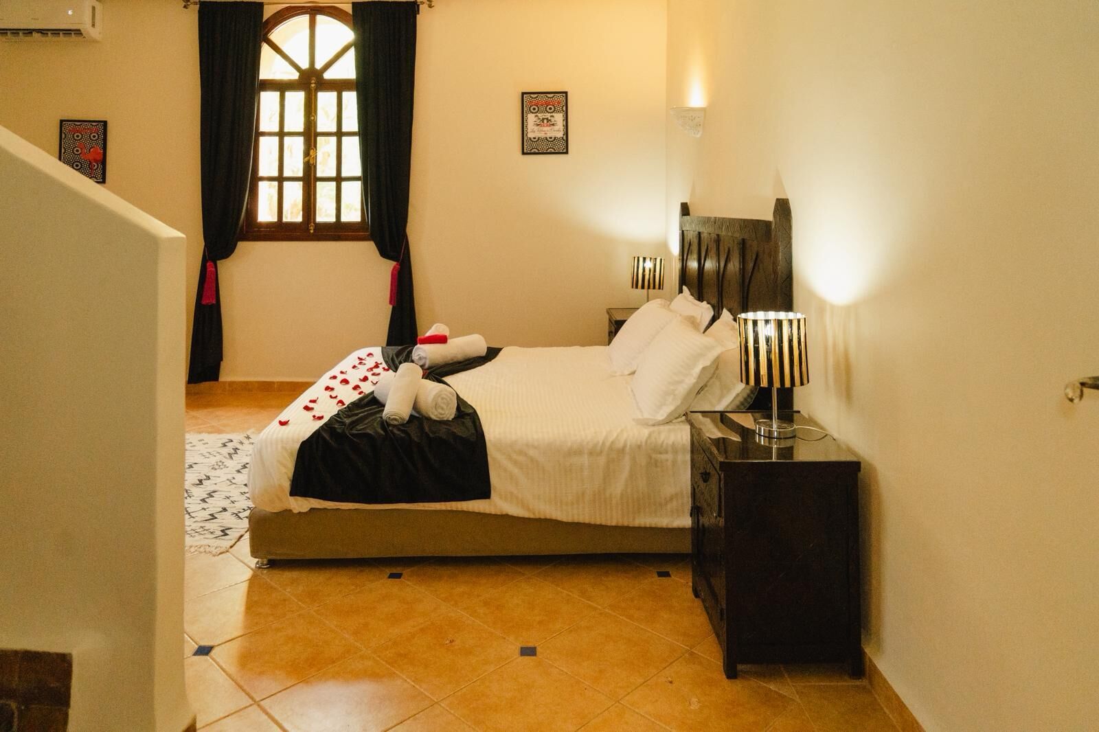 A hotel room with a bed, a nightstand, a lamp, a window with curtains, and a wall-mounted picture.