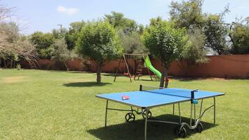 A blue table tennis table with wheels, a swing set, and trees in a grassy yard.
