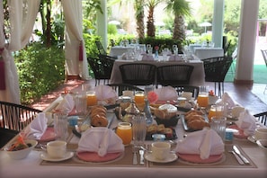 A breakfast setting with tables set for dining, including plates, glasses, and a variety of food items. - HOTEL BOUTIQUE PINK LAGOON (Ghmate)