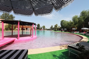 Una piscina con un deck rosa, rodeada de sillas de descanso y sombrillas a rayas.
