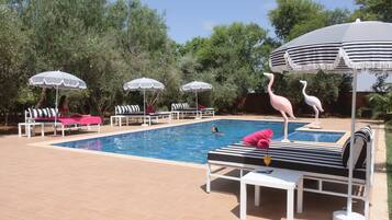 A swimming pool with lounge chairs and striped umbrellas, surrounded by trees.