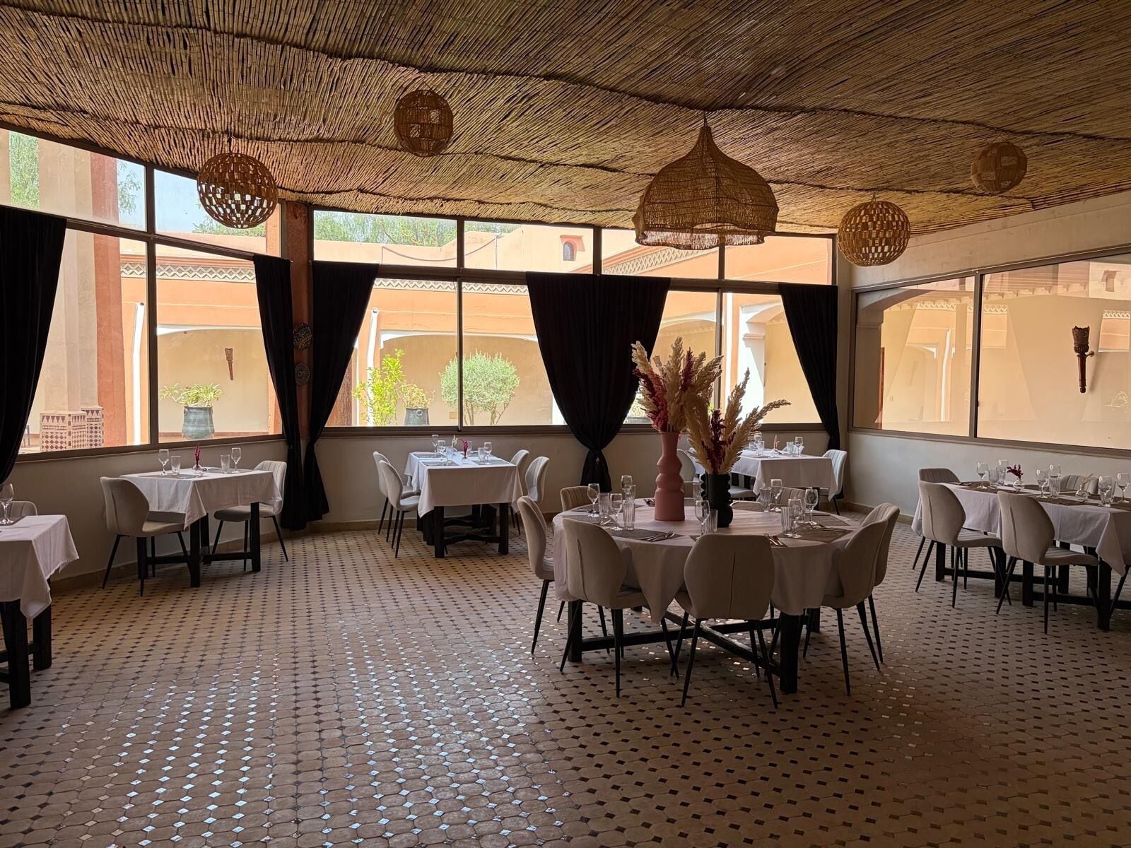 Un restaurante con varias mesas, piso estampado y amplios ventanales con cortinas.