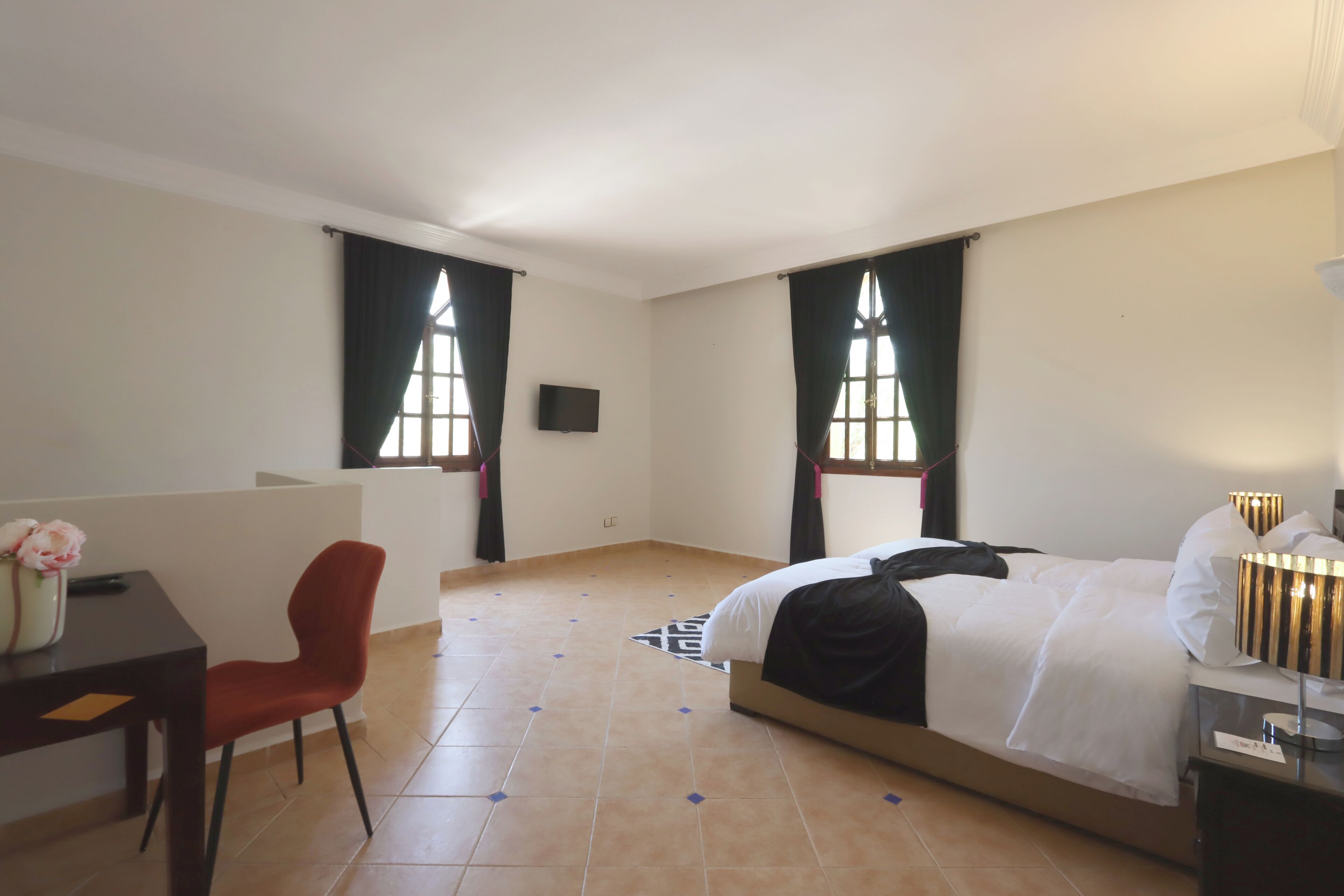 Une chambre d’hôtel avec un lit, un bureau, une chaise et deux fenêtres avec des rideaux.