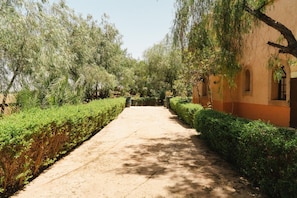 A pathway flanked by neatly trimmed hedges and trees, leading to a building with arched windows and a traditional facade. - Hotel Boutique Les Relais De L'Ourika (Marrakech)
