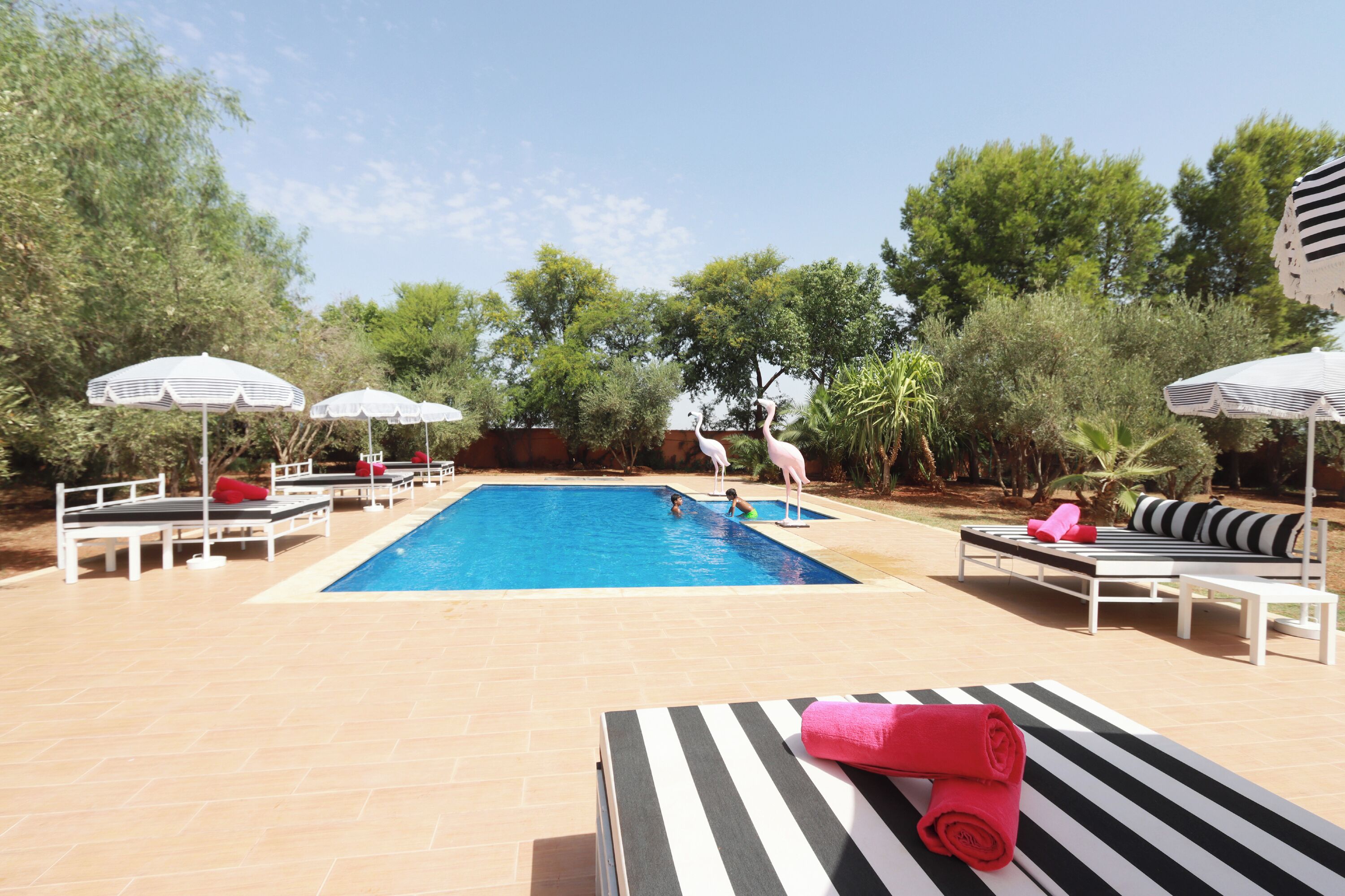Una piscina con sillones de descanso y sombrillas, rodeada de vegetación.