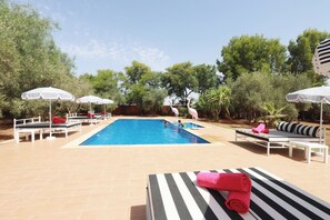 A swimming pool with lounge chairs and umbrellas, surrounded by greenery.