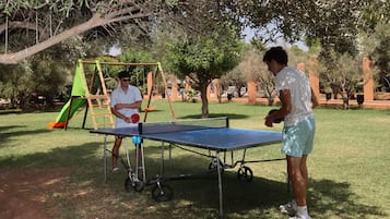An outdoor table tennis setup in a park with a swing set and trees in the background.