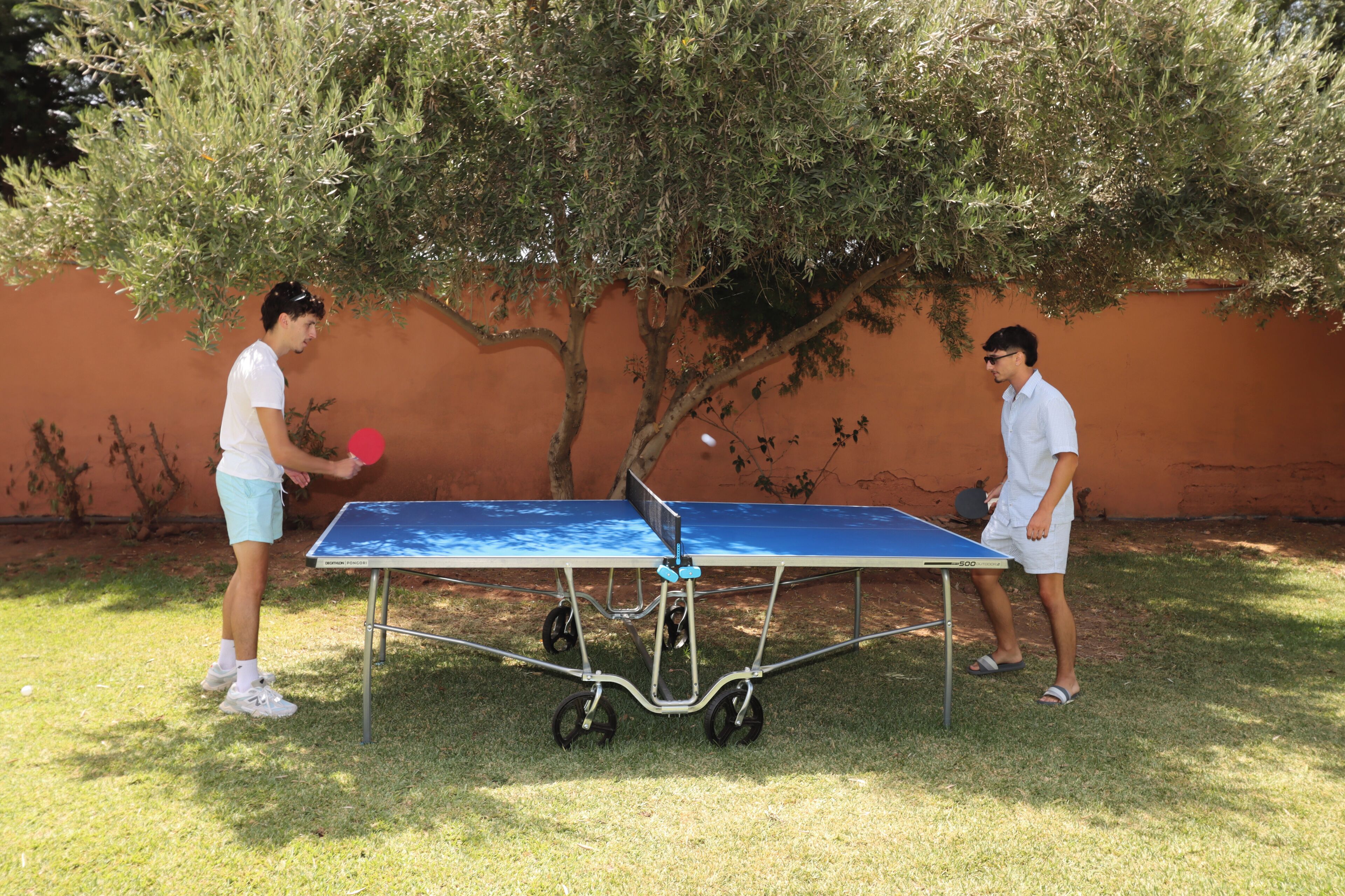 Dos personas jugando ping pong al aire libre, con una mesa y una red.