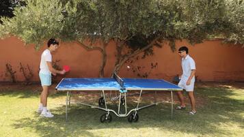 Dos personas jugando ping pong al aire libre, con una mesa y una red.