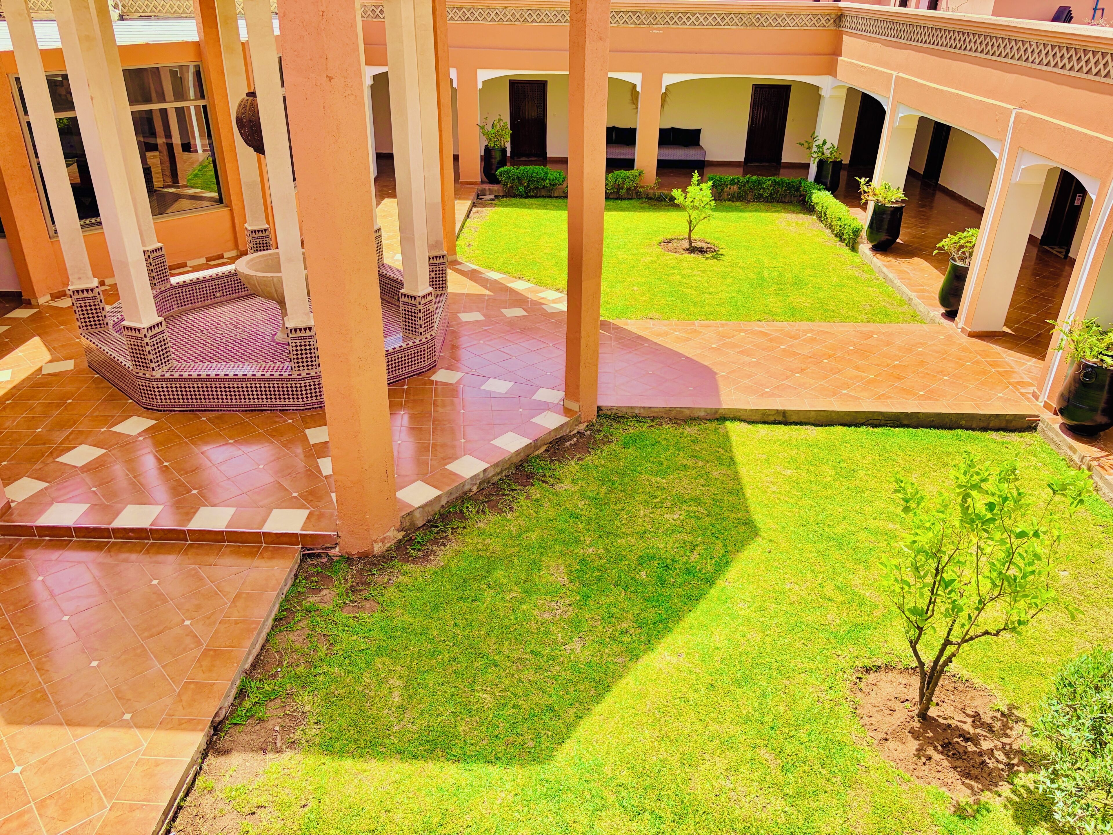 A courtyard with a tiled floor, a central lawn area, and a seating area with a patterned floor.