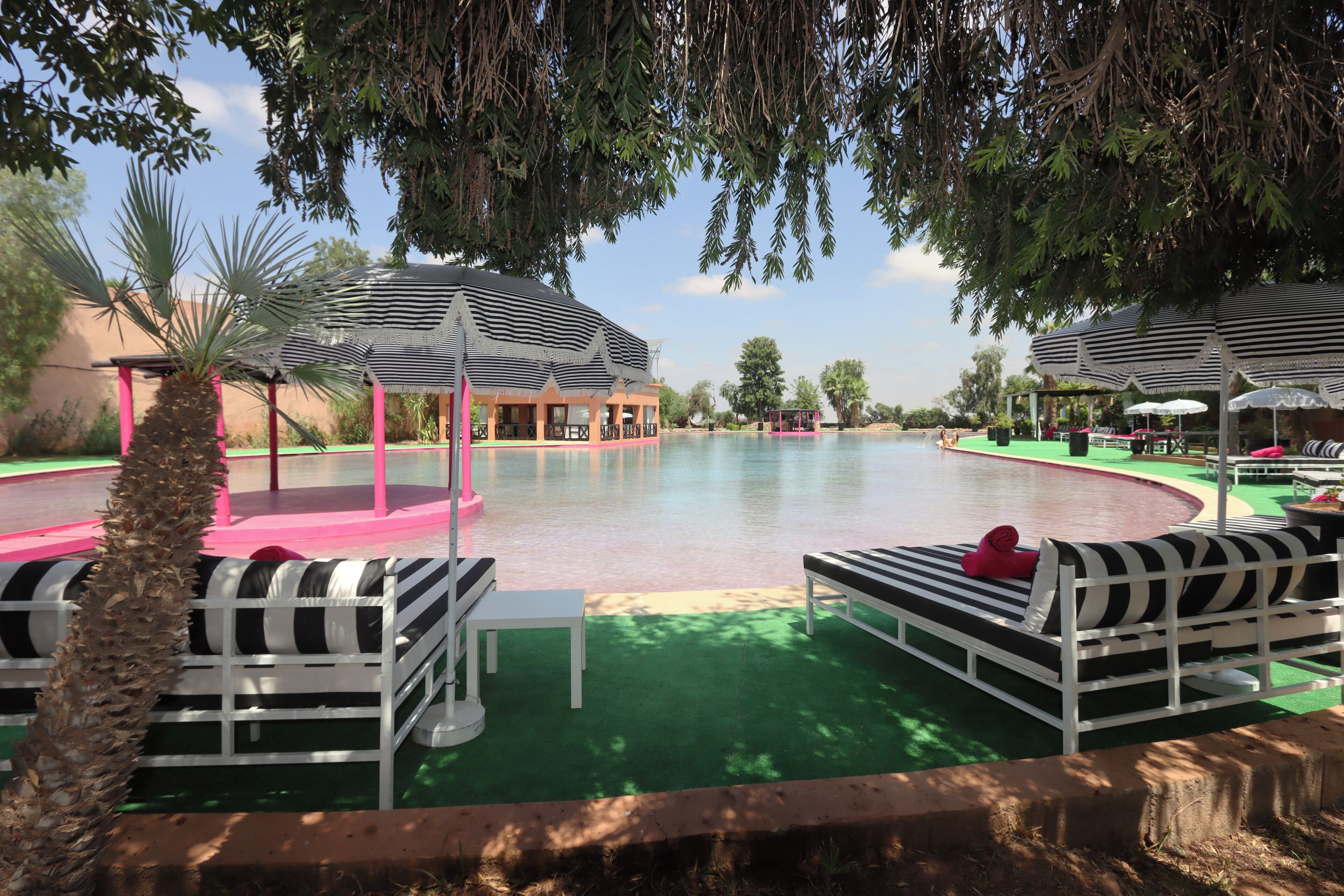 A pool area with striped umbrellas, lounge chairs, and a building with pink columns.