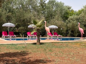 A swimming pool with lounge chairs and umbrellas, surrounded by trees and a flamingo statue. - HOTEL BOUTIQUE PINK LAGOON (Ghmate)