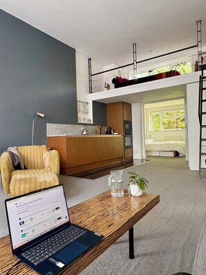 Ein moderner Wohnraum mit Laptop auf einem Holztisch, einer Couch und einer Küchenzeile mit Balkon.