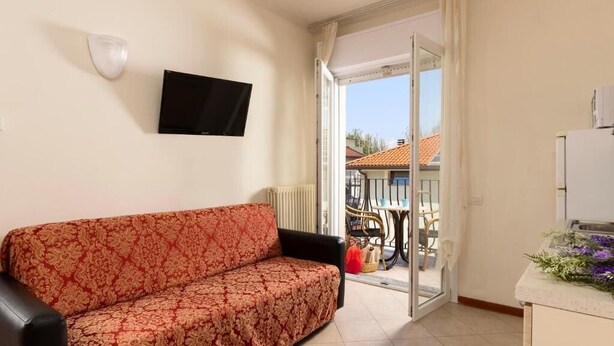 A living room with a sofa, a television, and a sliding glass door leading to an outdoor area with a table and chairs.