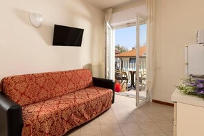 A living room with a sofa, a television, and a sliding glass door leading to an outdoor area with a table and chairs. - Residence 1 Studio&Suites (Rimini)
