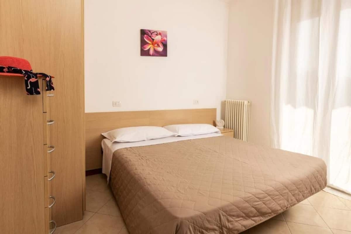 Une chambre à coucher avec un lit, une armoire en bois, un radiateur et une fenêtre avec des rideaux.