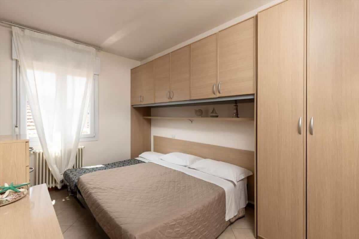 Une chambre à coucher avec un lit, une armoire, un radiateur et une fenêtre avec des rideaux.