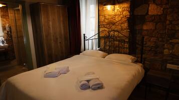Een hotelkamer met een bed, een stenen muur, een metalen hoofdbord en een badkamer met een wastafel en spiegel.