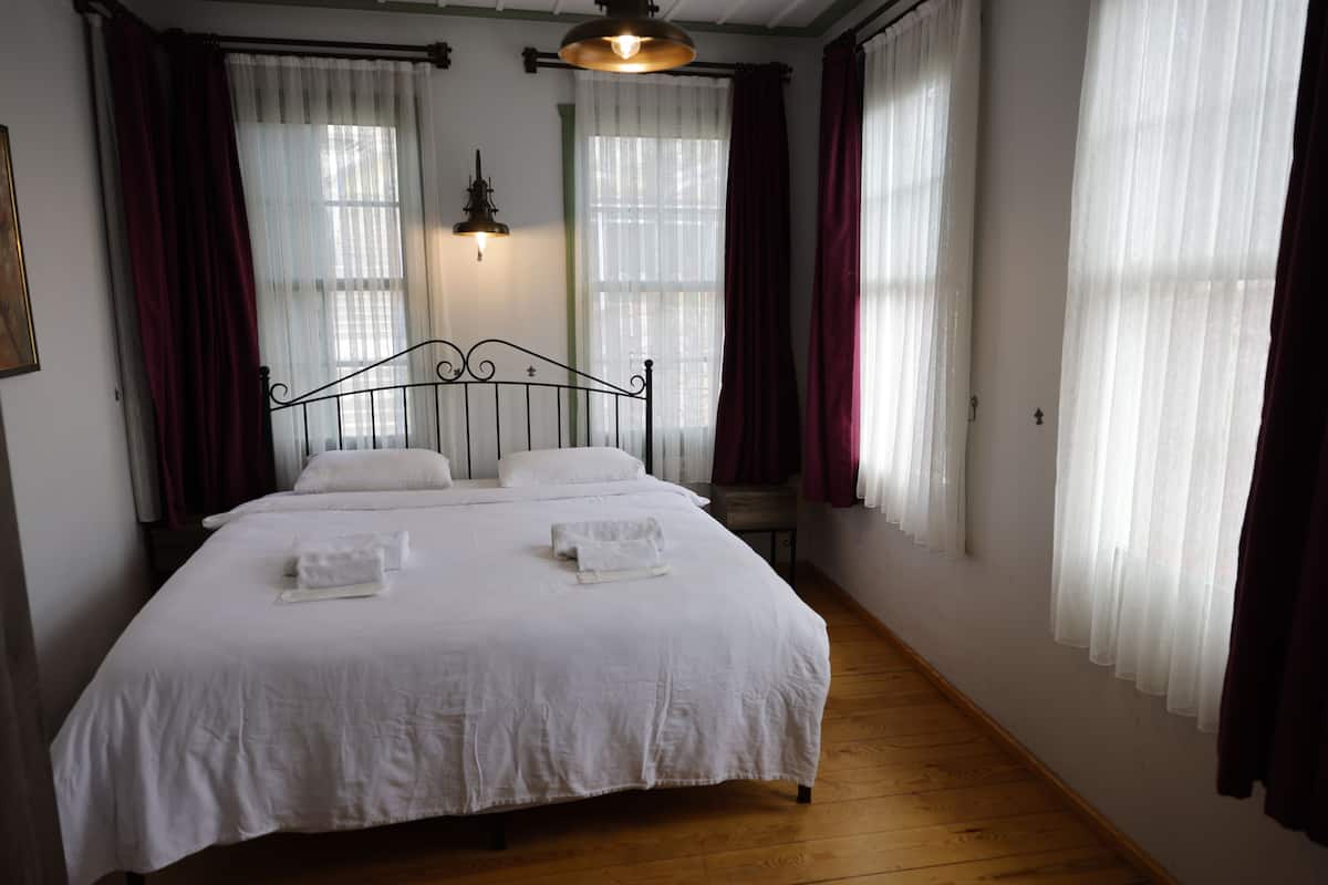 Un dormitorio con una cama grande, dos mesitas de noche, una lámpara de pared y cortinas translúcidas.
