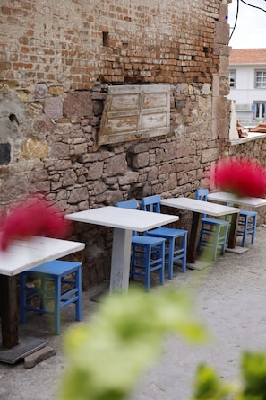 Outdoor seating with tables and chairs, a stone wall, and a building in the background.