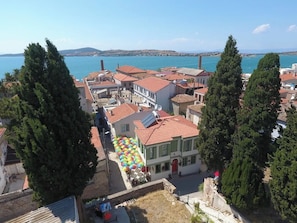 A coastal town with red-roofed buildings, a clear blue sea, and a view of distant hills. - My Flora Pansiyon (Ayvalık / Balıkesir)