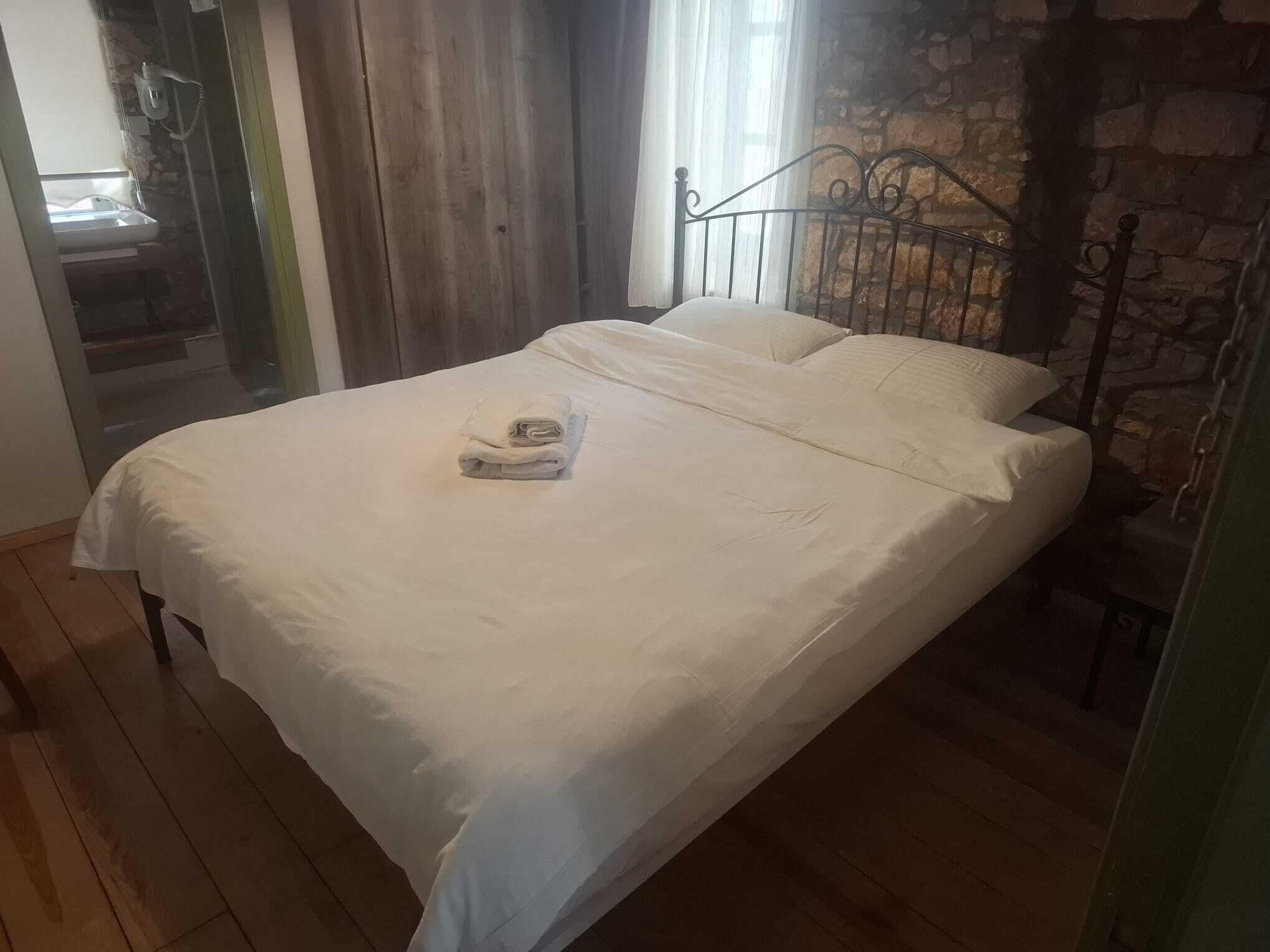A bed with white linens, a metal headboard, and a stone wall.