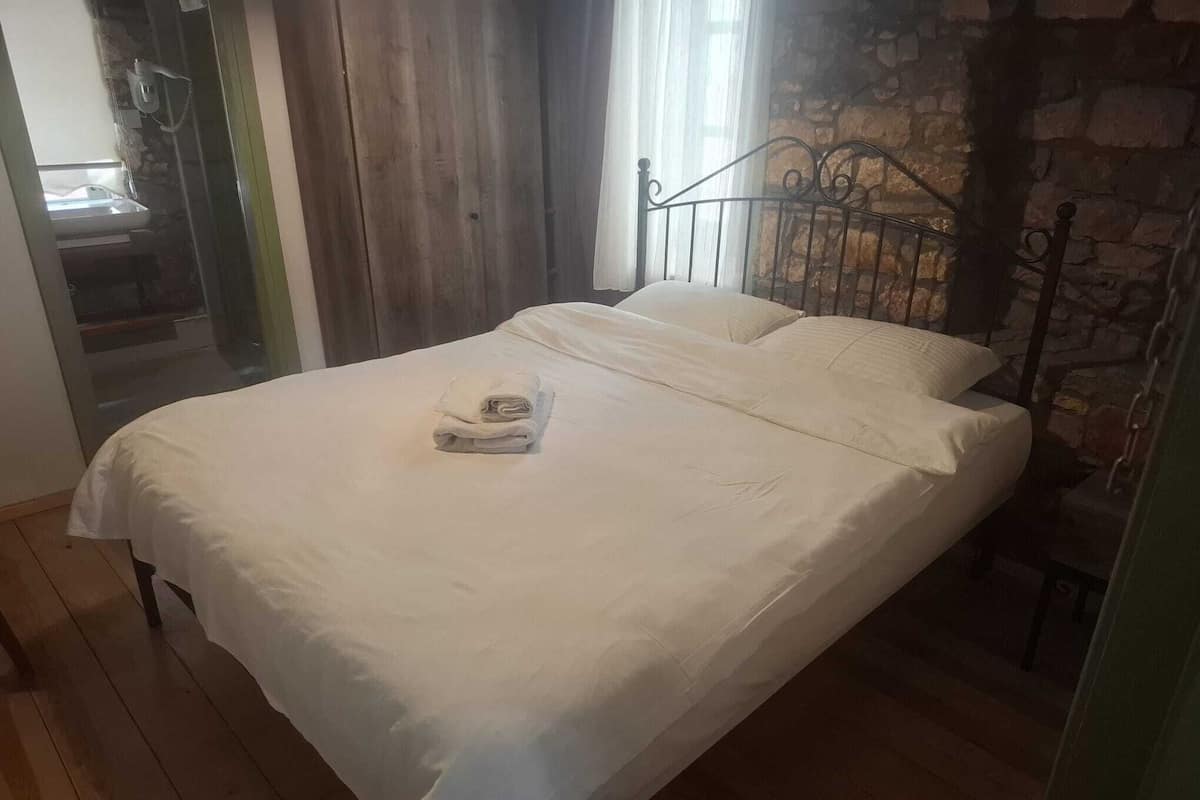 Una cama con sábanas blancas, cabecero de metal y pared de piedra.