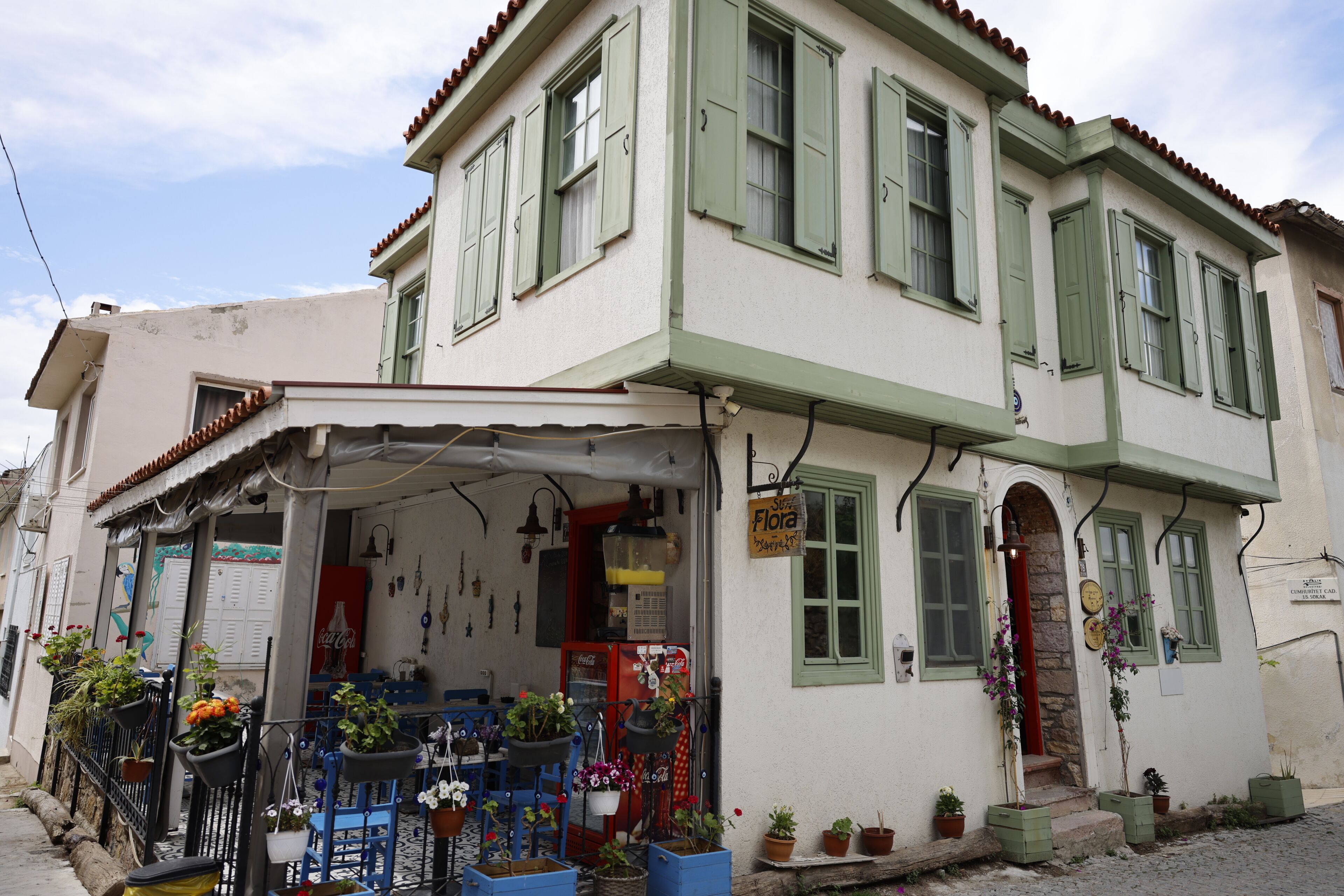 A two-story building with a shop on the ground floor, potted plants, and a sign indicating a flower shop.