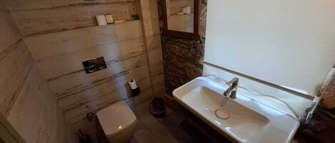 Een badkamer met een houten wand, een wit wastafelmeubel en een toilet.