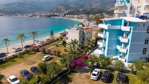 A coastal hotel with a view of the sea, a parking area, and a garden with flowering plants. - Blue Stay Hotel (Himarë)