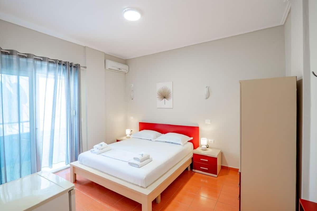 Habitación de hotel con cama, mesitas de noche, aire acondicionado, armario y ventana con cortinas.
