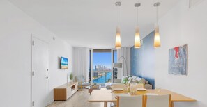 Ein modernes Wohnzimmer mit Essbereich, großen Fenstern und Blick auf die Stadt, sparsam eingerichtet.