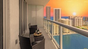 Ein Balkon mit Blick auf eine Skyline bei Sonnenuntergang, einem Esstisch mit Stühlen und einem Pool.
