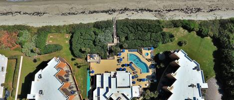 An aerial view of a coastal hotel with a swimming pool, multiple guest rooms, and a beach view.