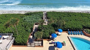 A rooftop pool area with blue umbrellas, lounge chairs, and a view of the ocean.