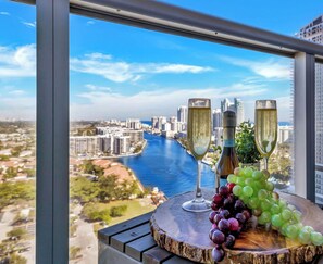 A balcony with a city view, two champagne flutes, and a bunch of grapes. - Elegant 1BR · Intracoastal View · Pool & Gym (Hallandale Beach)