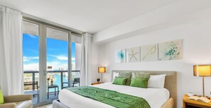 Ett hotellrum med en stor säng, två sänglampor, utsikt över staden och konstverk på väggen.