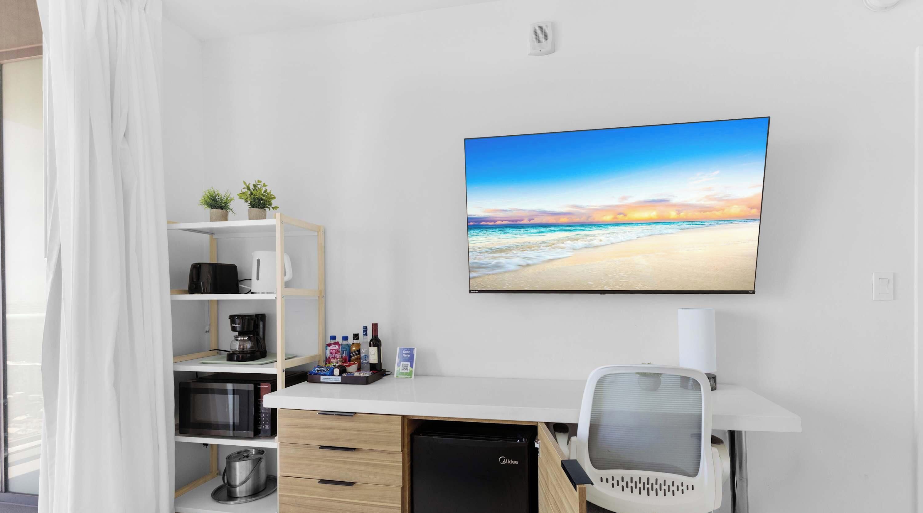 Ein modernes Zimmer mit Schreibtisch, Regalen, einer Mikrowelle, einer Kaffeemaschine, einem Kühlschrank und einem großen Fenster mit weißen Vorhängen.