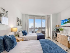 Ein modernes Hotelzimmer mit Bett, Nachttisch, Lampe und Blick auf die Stadt durch große Fenster.